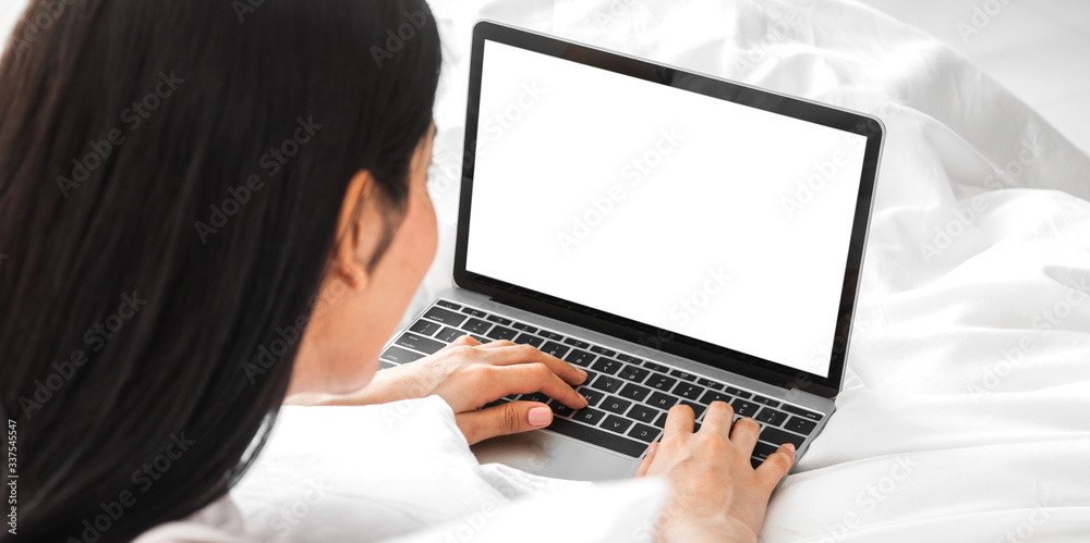 Young asian woman relaxing using laptop computer with white mockup blank screens in the bedroom at home. Young creative girl working and typing on keyboard.work from home concept Young asian woman relaxing using laptop computer with white mockup blank screens in the bedroom at home. Young creative girl working and typing on keyboard.work from home concept