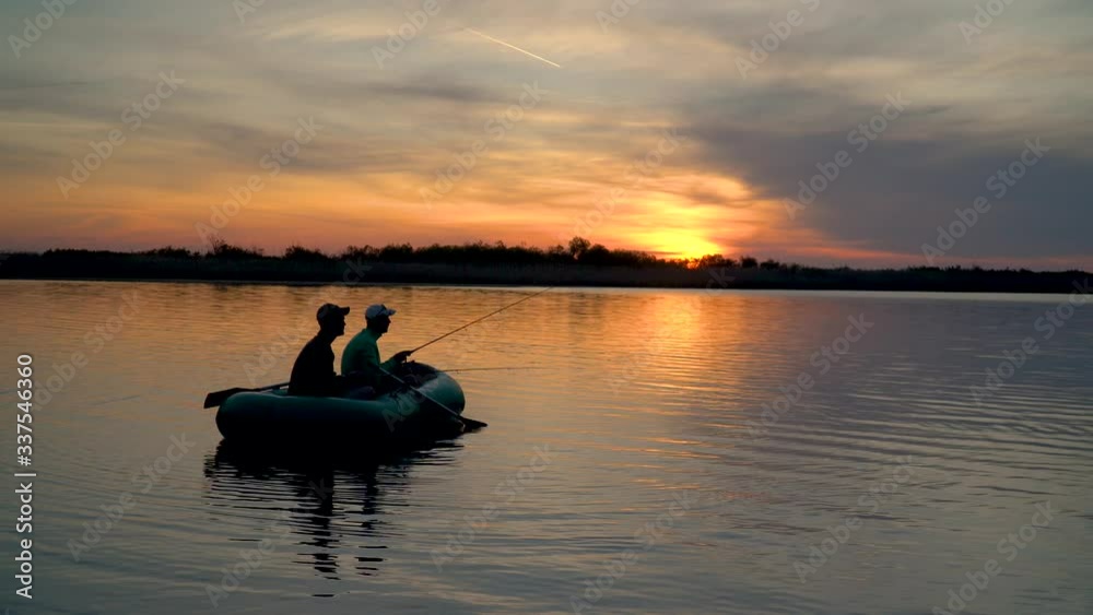 Two fishermen in the rays of the sunset catch fish from an inflatable boat Two fishermen in the rays of the sunset catch fish from an inflatable boat
