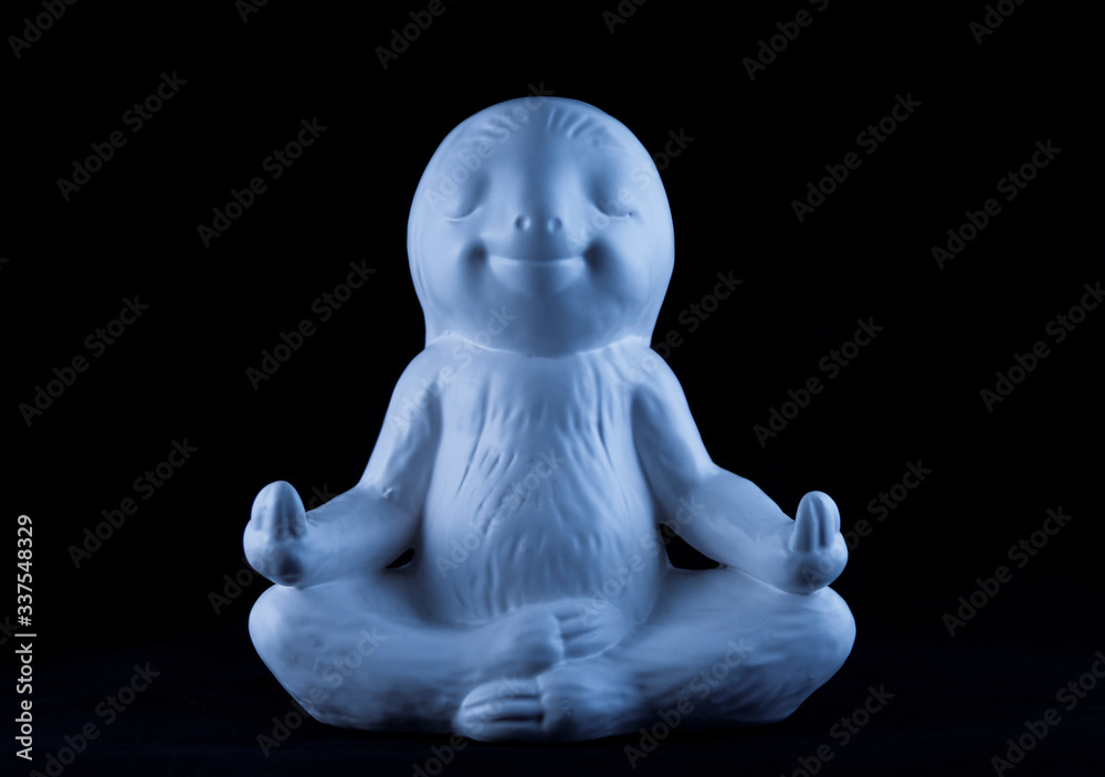 Blue smiling and calm looking sloth ornament sitting in the lotus meditating position against a black background. Blue smiling and calm looking sloth ornament sitting in the lotus meditating position against a black background.