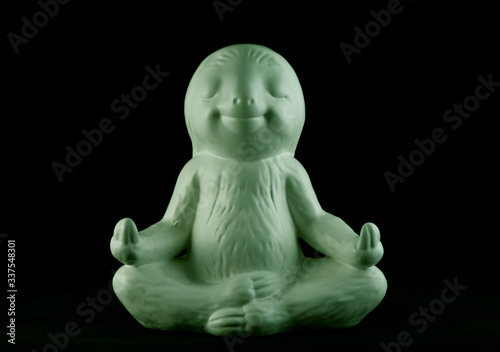 Green smiling and calm looking sloth ornament sitting in the lotus meditating position against a black background.