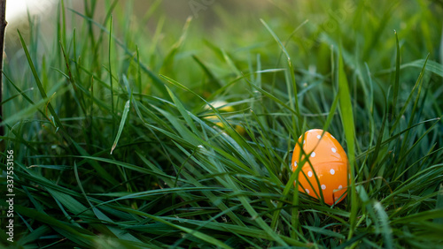 Orange polka dotted Easter egg laying in the grass at sunset