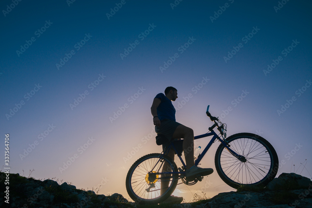 Silhouette of a fit male mountain biker riding his bike uphill on rocky harsh terrain on a sunset. Silhouette of a fit male mountain biker riding his bike uphill on rocky harsh terrain on a sunset.