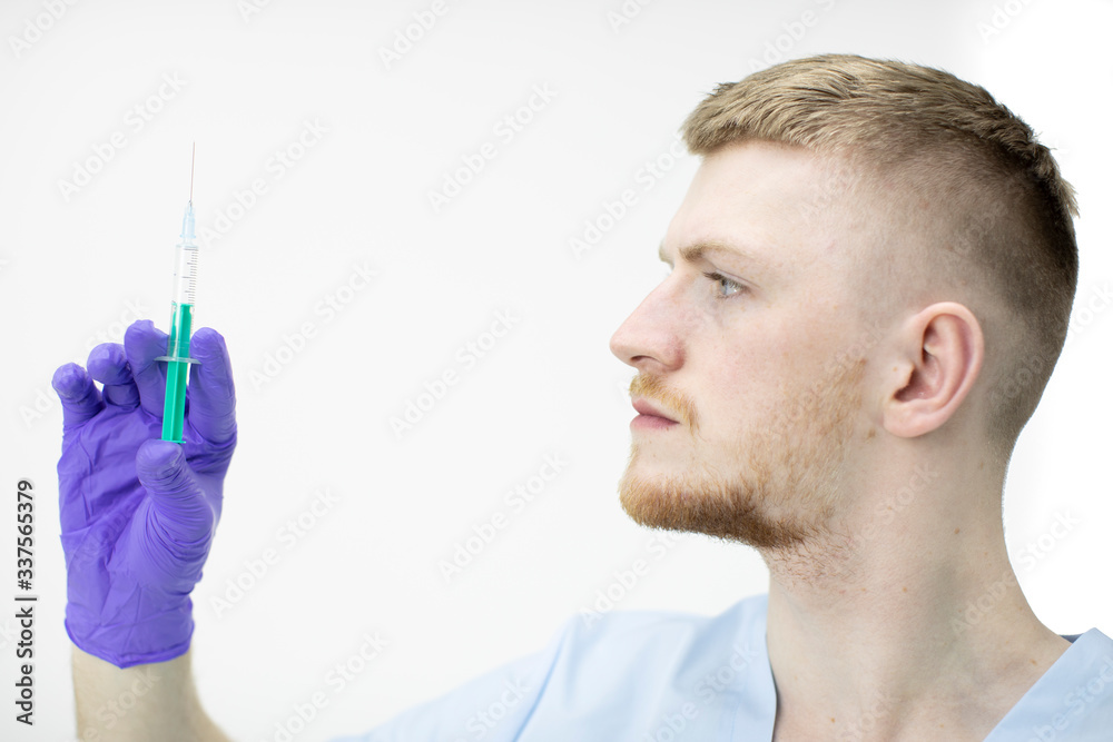 Young attractive male lab technician assistant in medical uniform and rubber gloves holding syringe with vaccine against covid-19. Stop spread of coronavirus global pandemic, biohazard protection Young attractive male lab technician assistant in medical uniform and rubber gloves holding syringe with vaccine against covid-19. Stop spread of coronavirus global pandemic, biohazard protection
