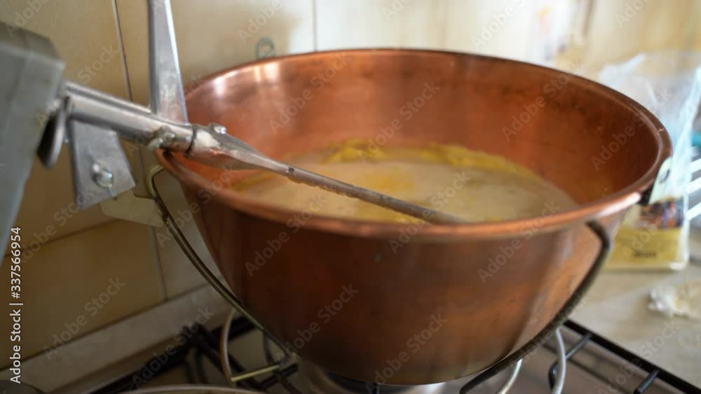 Traditional rustic preparation of yellow polenta in copper cauldron with stirring metal whisk, corn flour mixing with boiling water, hot maize porridge is a typical dish of northern Italy. Italian Traditional rustic preparation of yellow polenta in copper cauldron with stirring metal whisk, corn flour mixing with boiling water, hot maize porridge is a typical dish of northern Italy. Italian