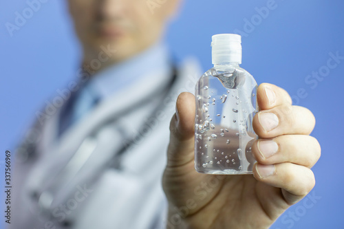 Close up sanitizer alcohol gel in hand to prevent spread of covid-19 coronavirus pandemic. Doctor in white lab coat and stethoscope on background. Focus on antiseptic. Personal hygiene concept