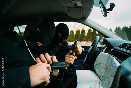 Tableau sur toile Bank robbers with their masks on pointing at the map prepared for robbing the bank,sitting in the car and waiting for the right time to rob
