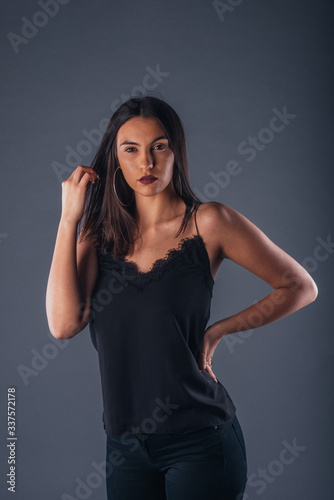 Young beautiful stylish girl posing in studio with one hand on the waist on a gray background © qunica.com