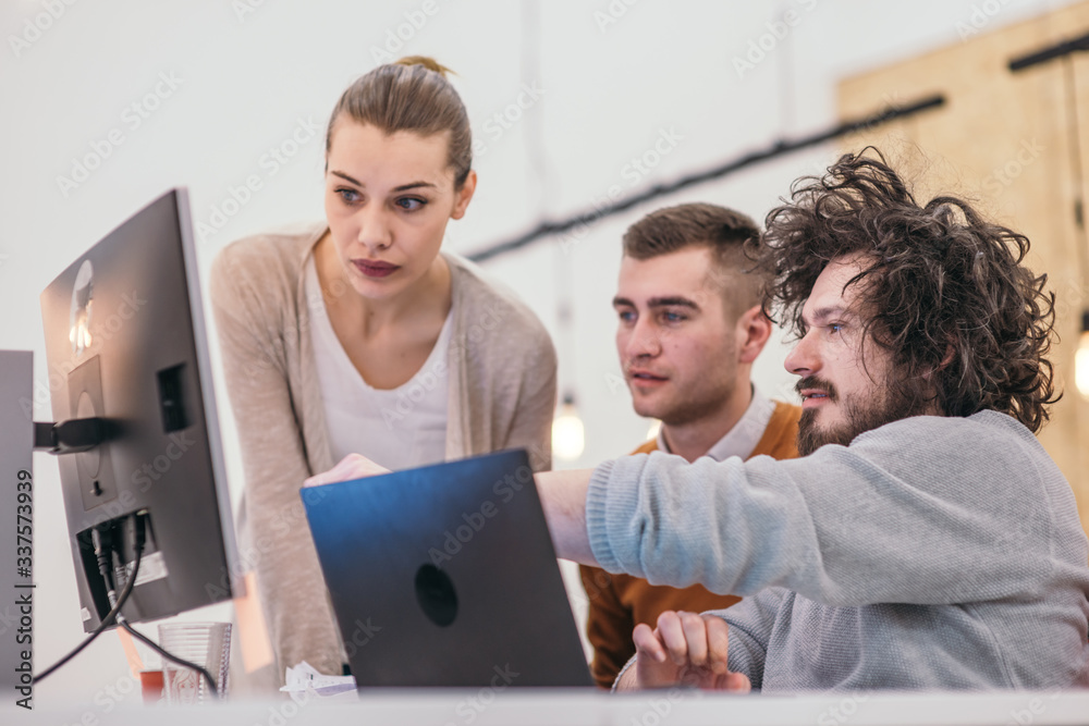 Coworkers, employees working and discussing a project they are preparing while typing on a laptop and looking at pc, computer. Coworkers, employees working and discussing a project they are preparing while typing on a laptop and looking at pc, computer.