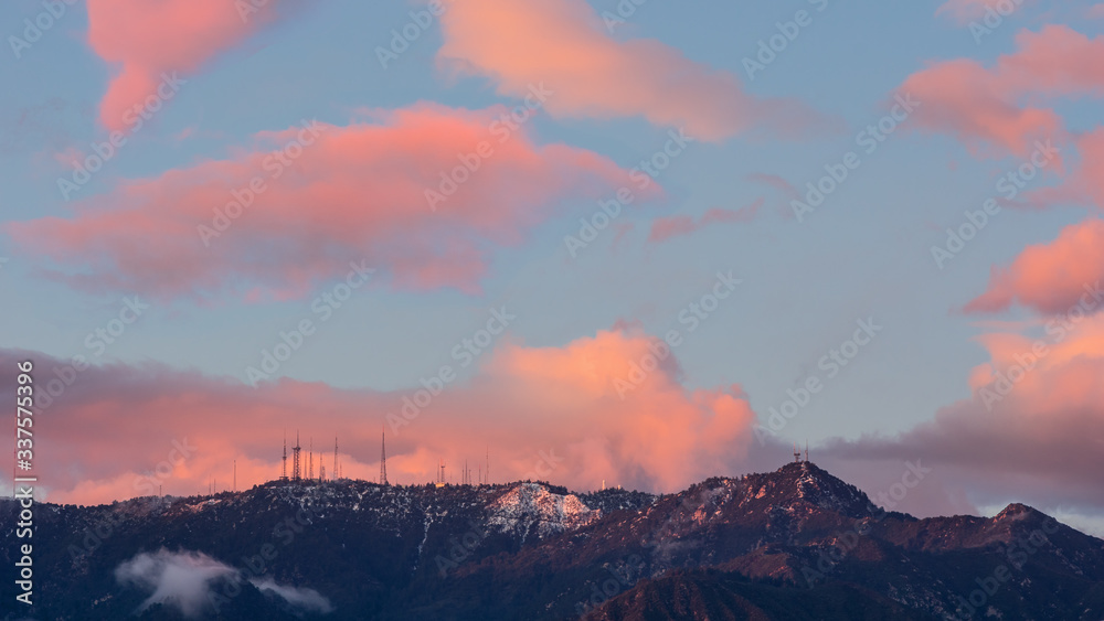 Panoramic image taken from Pasadena in Los Angeles County showing Mt Wilson on the San Gabriel Mountains after light snowfall. Blue dusk sky and pink clouds.
