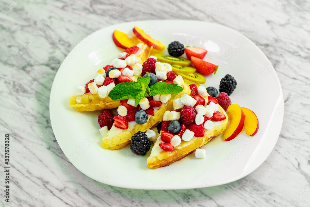 Belgian waffles with nuts, chocolate and fruit on a white plate, beautiful serving