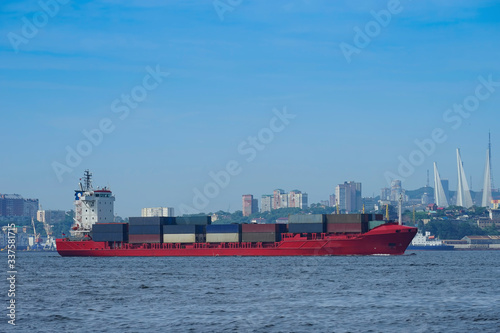Red container ship on the background of the urban landscape.
