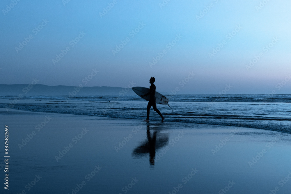 Man with surfboard walking on beach at dusk