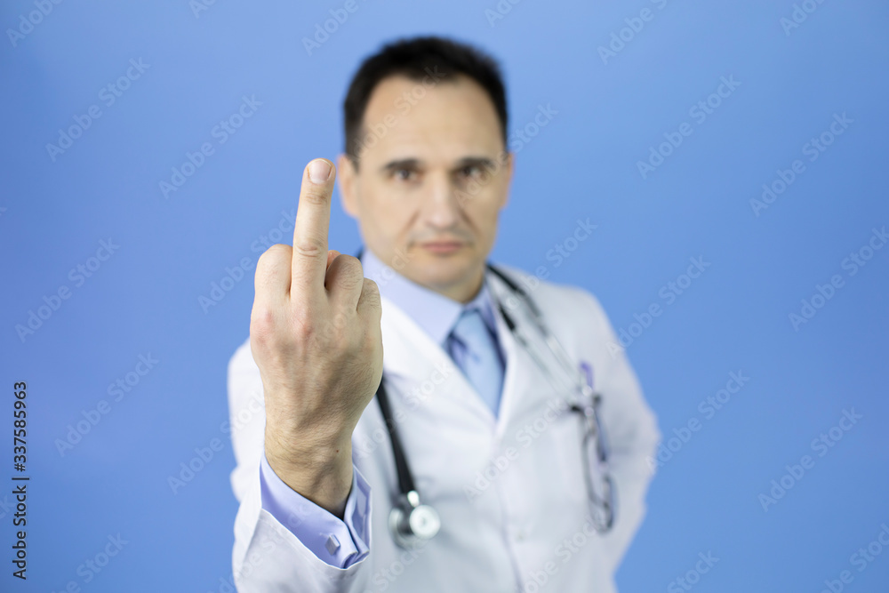 Middle-aged doctor in white coat and stethoscope shows middle finger doing fuck you, provocation, rude attitude, blue background. Medicine against disease, coronavirus pandemic and infections concept Middle-aged doctor in white coat and stethoscope shows middle finger doing fuck you, provocation, rude attitude, blue background. Medicine against disease, coronavirus pandemic and infections concept