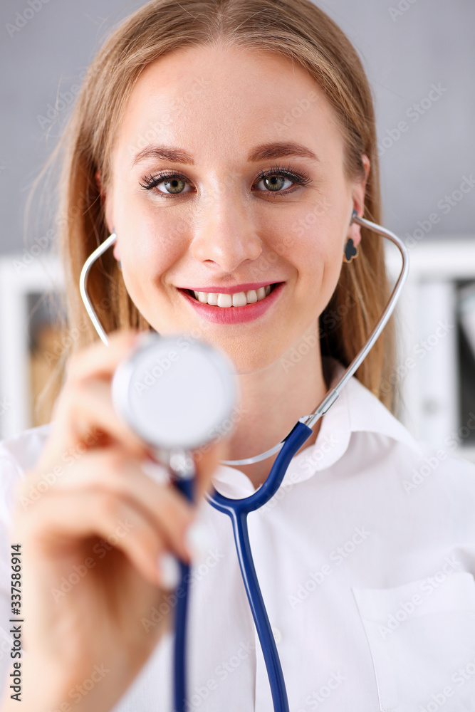 Beautiful smiling female doctor hold in arm stethoscope head going to listen patient. Medic shop or store, physical, disease prevention, er consultant, 911, pulse measure, healthy lifestyle concept Beautiful smiling female doctor hold in arm stethoscope head going to listen patient. Medic shop or store, physical, disease prevention, er consultant, 911, pulse measure, healthy lifestyle concept