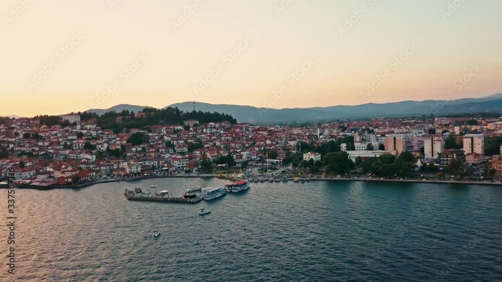 Panoramic view of Ohrid (city) at dusk as the sky is filled with a pink and orange haze. The sunset reflects onto Lake Ohrid in North Macedonia. Panoramic view of Ohrid (city) at dusk as the sky is filled with a pink and orange haze. The sunset reflects onto Lake Ohrid in North Macedonia.