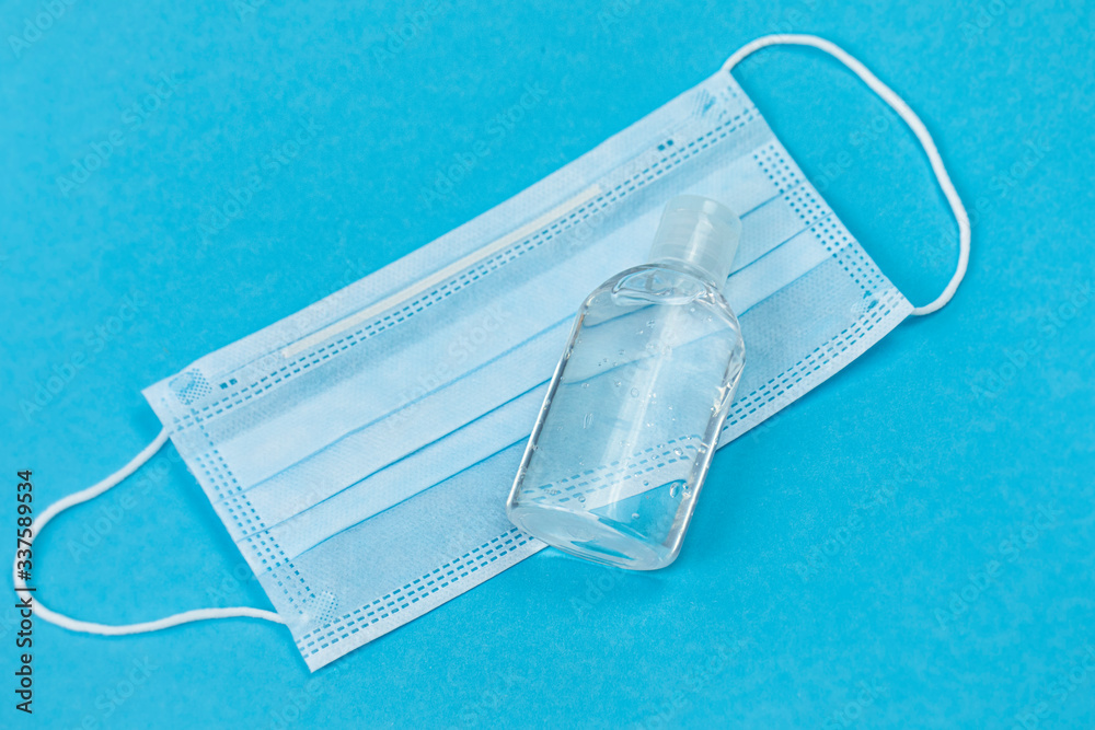 Hand sanitizer and medial mask isolated, blue background, covid-19 coronavirus