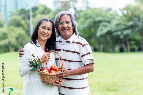 happy asian senior couple holding basket apple and flower picnic in public park.