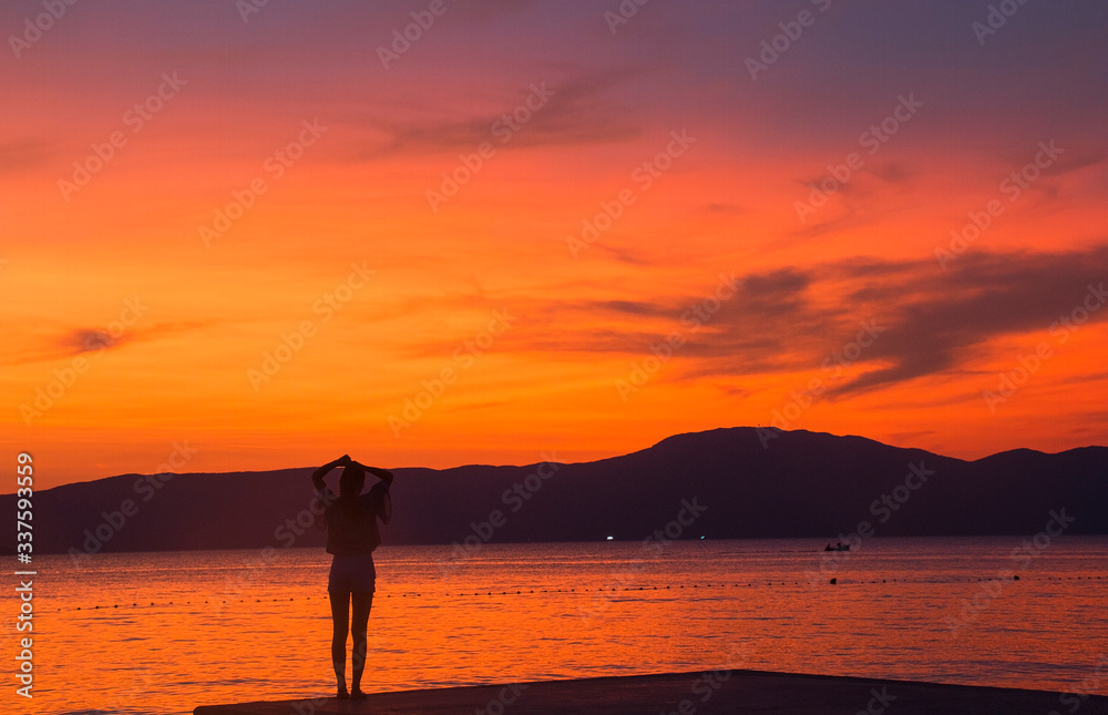 silhouette of a girl sitting on a pier at sunset of the sea