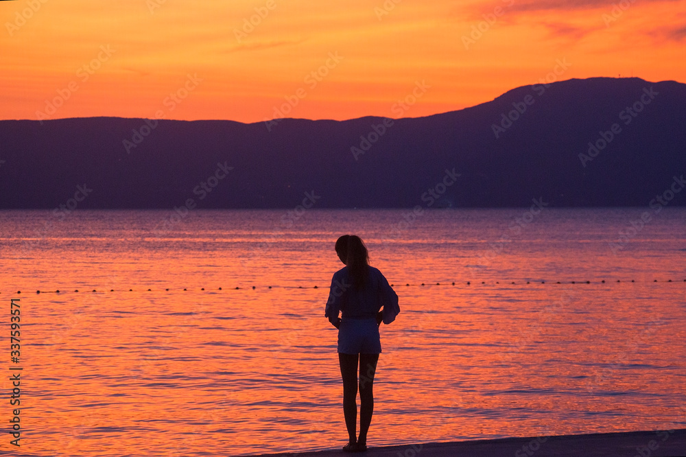 silhouette of a girl sitting on a pier at sunset of the sea
