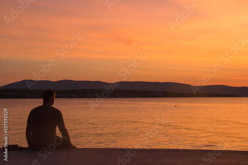 silhouette of a man sitting on a pier at sunset of the sea