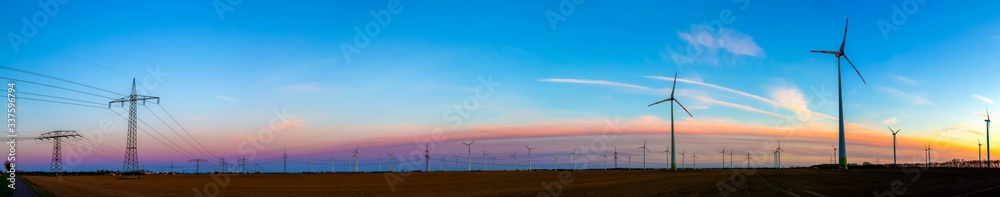 Obraz premium viele Windräder bei Sonnenuntergang stehen auf einem Feld und produzieren Strom
