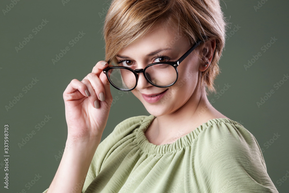Studio portrait of young woman in green shirt wearing reading glasses and looking at camera. 
