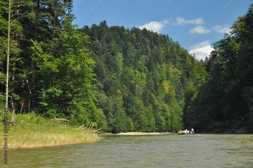 Rafting on the Dunajec River in the Pieniny National Park on wooden folding shuttles tied with a rope. Rafters paddling on a rapid stream with a rocky bottom and strong river current. Rafting on the Dunajec River in the Pieniny National Park on wooden folding shuttles tied with a rope. Rafters paddling on a rapid stream with a rocky bottom and strong river current.