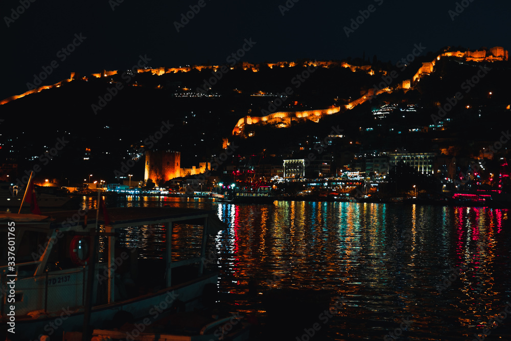 Night view image of old city near sea with ancient castle, houses and stone walls scenery between lights from Alanya Antalya Turkey