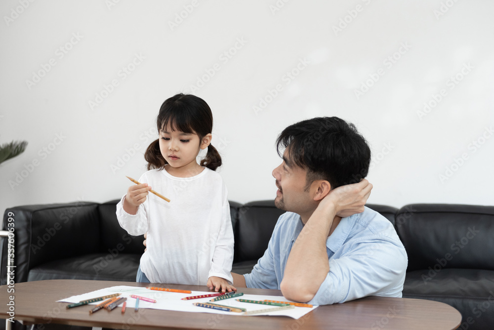 A pair of young Asian father and daughter are drawing in the living room A pair of young Asian father and daughter are drawing in the living room