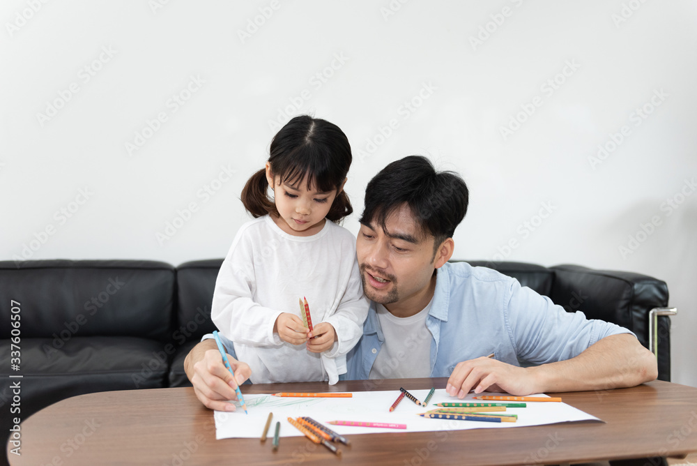 A pair of young Asian father and daughter are drawing in the living room A pair of young Asian father and daughter are drawing in the living room
