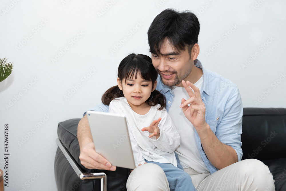 A pair of young Asian father and daughter are using tablet in the living room A pair of young Asian father and daughter are using tablet in the living room