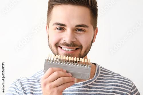 Young man with teeth color samples on white background