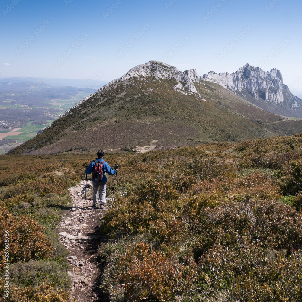 Female hiker descending a mountain and view over peak Recilla in the Cantabria mountain range between La Rioja and Alava, Basque Country, Spain