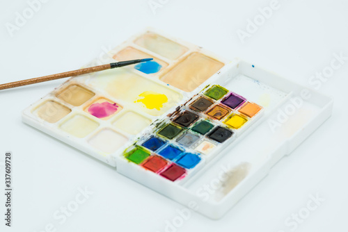 Palette of watercolors on white background. Brush mixing colors, blue, yellow and magenta in the palette.