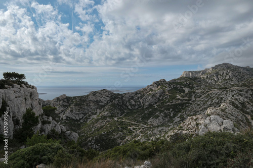 Mountains with green grass and grey rocks near the sea. Blue sky and white clouds.