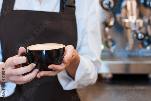 Closeup female hands are holding cup of aromatic coffee. Barista woman prepared, brewed espresso, americano. Girl made latte cappuccino using professional machine in cafe, restaurant. Hot drinks.