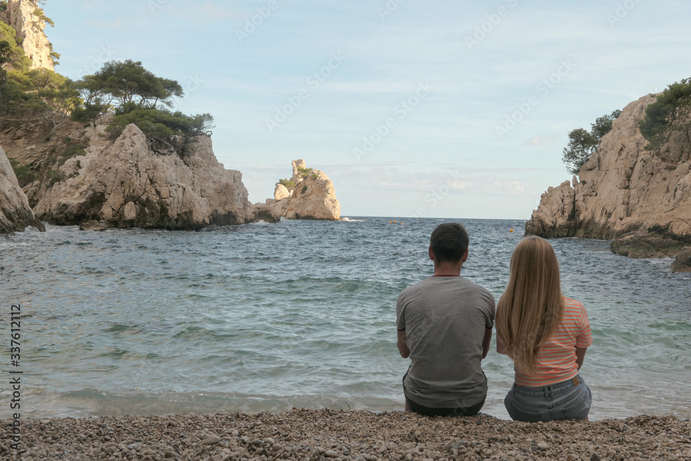 A couple is sitting in the mountains with green grass and grey rocks near the sea.