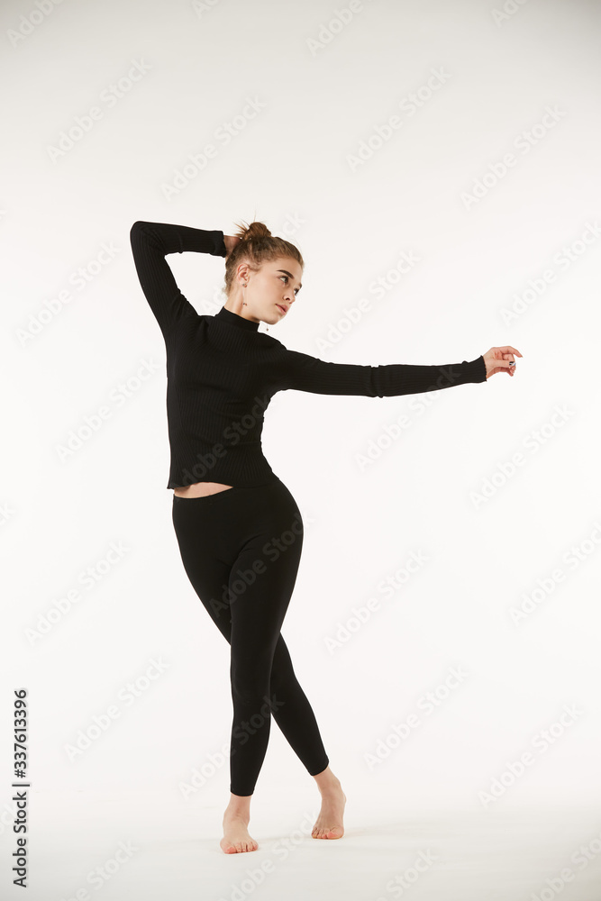 A girl in black clothes on a white isolated background performs dance and ballet poses and movements.