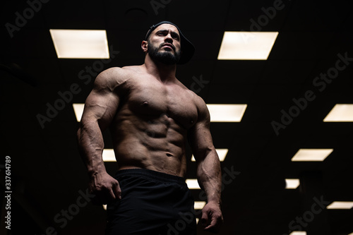 muscular aggressive young male with beard wearing cap in dark sport gym with yellow lamps light photo