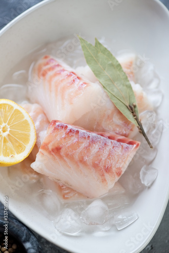 Close-up of uncooked iced codfish fillet with lemon and bay leaves, vertical shot, selective focus