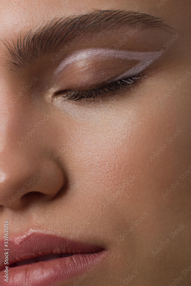 Close up half portrait of a face with beautiful skin and nude makeup, eyeliner and long eyelashes, puffy natural lips and white flowers. Fashion photography. Cosmetology and spa. Freshness of spring Close up half portrait of a face with beautiful skin and nude makeup, eyeliner and long eyelashes, puffy natural lips and white flowers. Fashion photography. Cosmetology and spa. Freshness of spring