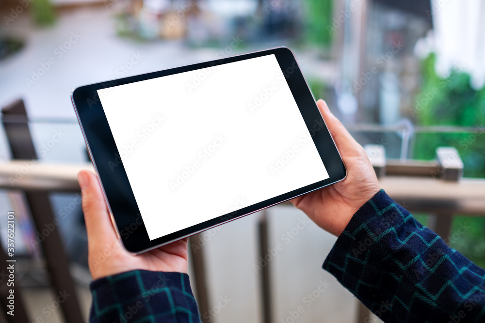 Mockup image of a woman holding black tablet pc with blank white desktop screen indoors