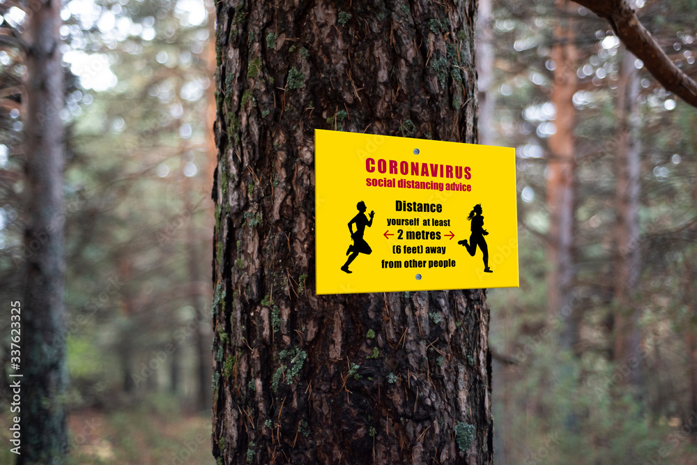 Fototapeta premium Social distancing advice for coronavirus. Outdoor sign in a park for coronavirus. Yellow sign in a park with social distancing advice. 