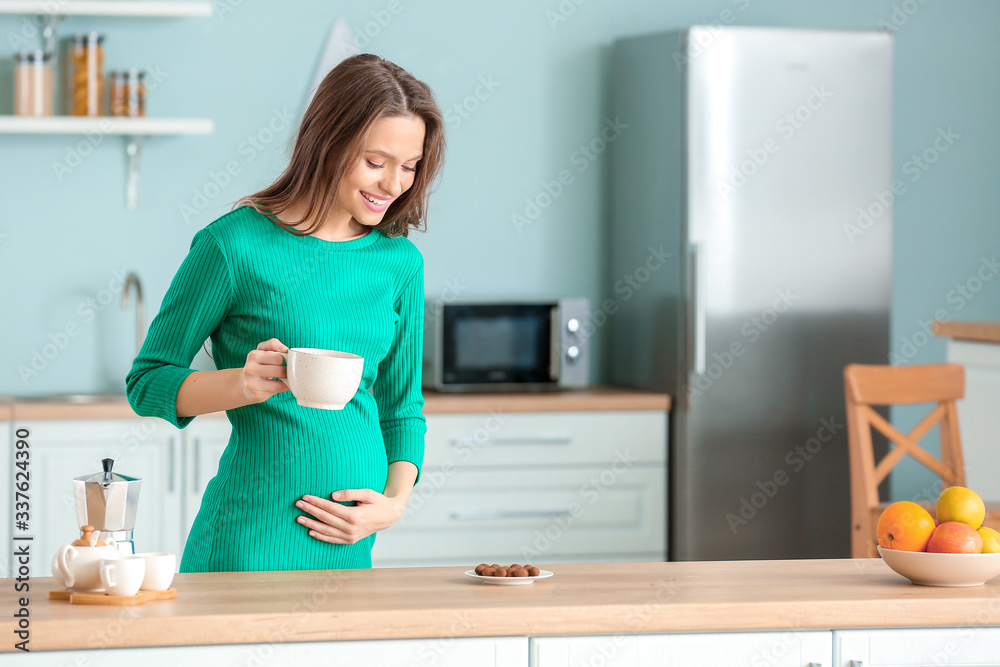 Beautiful pregnant woman with chocolate and tea in kitchen Beautiful pregnant woman with chocolate and tea in kitchen