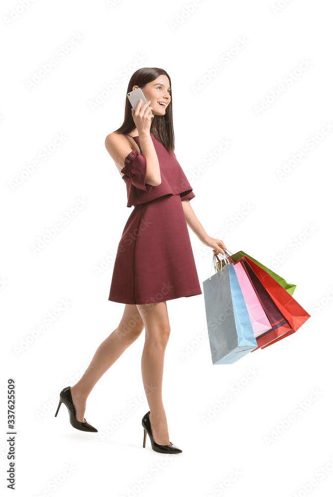 Beautiful young woman with shopping bags talking by mobile phone on white background