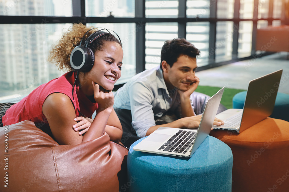 caucasian businesswoman and businessman in smart casual wear listening music from headphone and another working on computer in creative office with smiling and happy face caucasian businesswoman and businessman in smart casual wear listening music from headphone and another working on computer in creative office with smiling and happy face