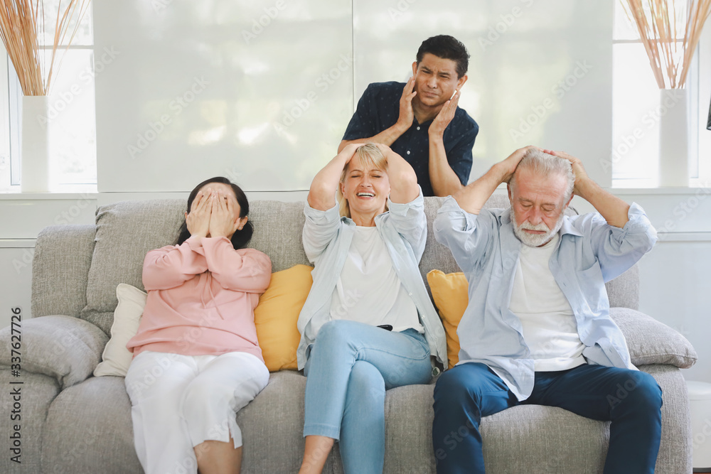Unhappy elder multiethnic family sitting and watching television on grey sofa in living room. They expressed sadness when the football team they cheered was beaten. Unhappy elder multiethnic family sitting and watching television on grey sofa in living room. They expressed sadness when the football team they cheered was beaten.