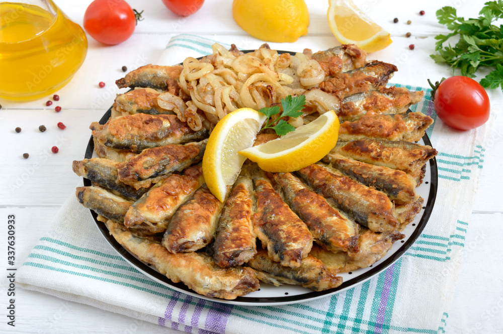 Fried capelin, sprats. Small fried fish on a plate on a white wooden background.