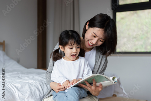 Young Asian mother is reading a book with her daughter