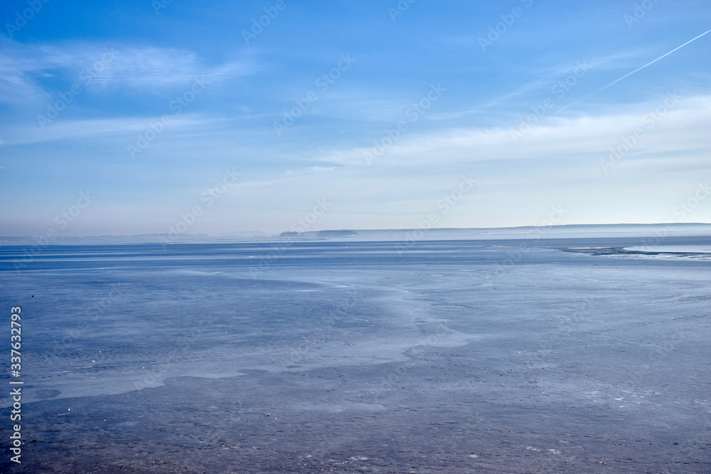 
The blue ice of a frozen reservoir merges with the sky in the early morning in winter